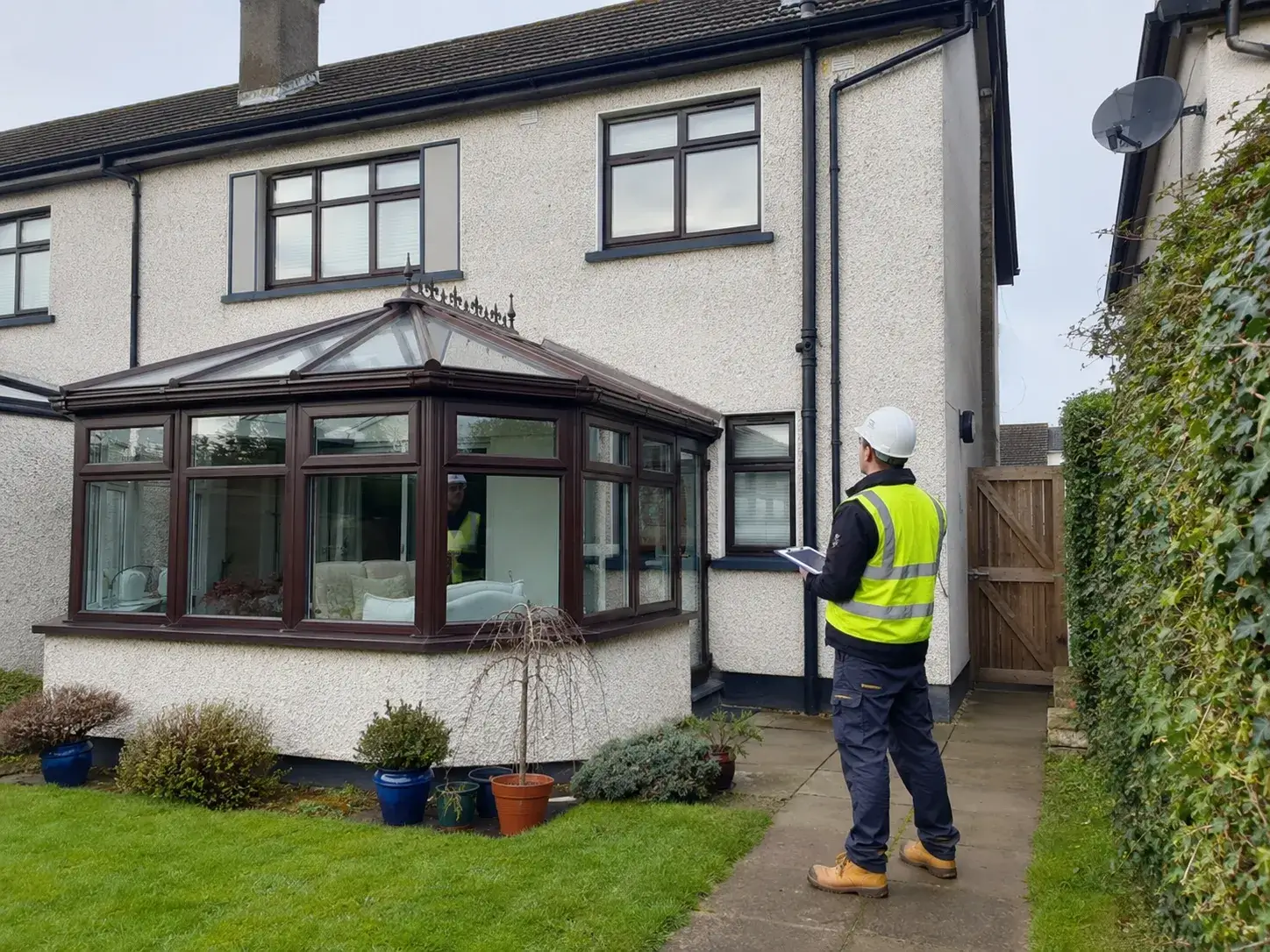 An Ainscaff contractor conducting a site survey at a residential property to plan scaffolding access around a garden conservatory and side gate.